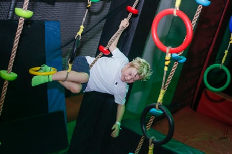 A boy traversing the Ninja Obstacle Course hanging rings at Flip Out UK