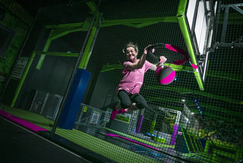 Girl jumping on trampoline after shooting ball through basketball hoop.