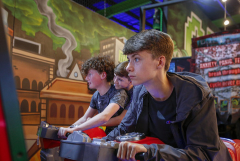 Older boy in indoor arcade at Flip Out Chester playing a game on motorbike with friends.