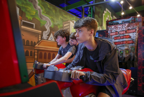 Older boy in indoor arcade at Flip Out Chester playing a game on motorbike with friends.