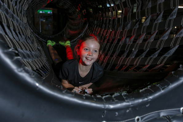 Smiling girl lying on black net structure at Flip Out play area.
