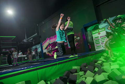 Girl leaping in the air towards a pit full of foam squares and a green light.