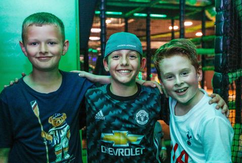 Three boys standing in front of Flip Out Soft Play, linking arms and smiling.