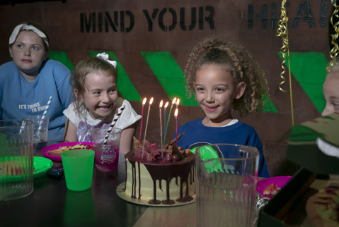 Girl excitedly about to blow birthday candles on her birthday cake with her excited friend and family around her.