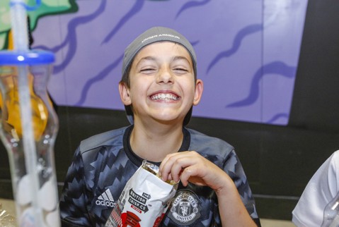 Boy grinning with his friend, eating a snack and next to a giant slushy cup.